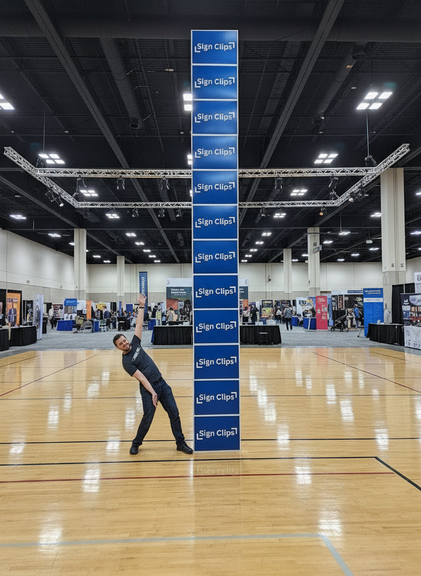 Person standing next to an 18ft tall yard sign tower in a convention center. 