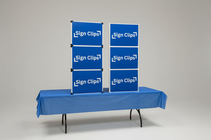 Two Sign Clip Table Top Display Towers on a table with a blue tablecloth. One Tower has white clips and the other has black clips.